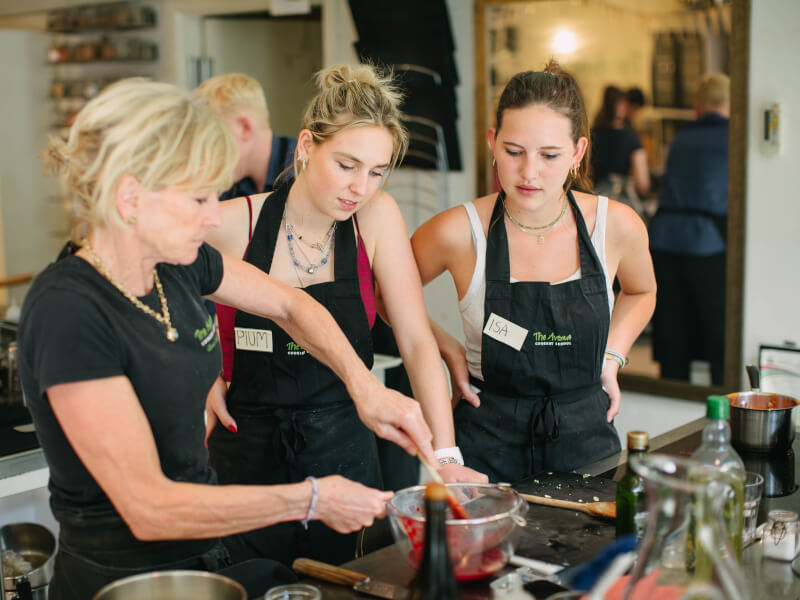 Chef teaching two young women to cook in an industrial kitchen